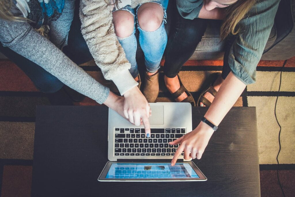 three person pointing the silver laptop computer showing online advertising