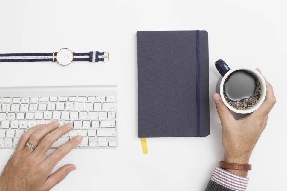 a desk with a keyboard, notebook, and coffee, representing the process of reviewing an SEO audit report and prioritizing fixes