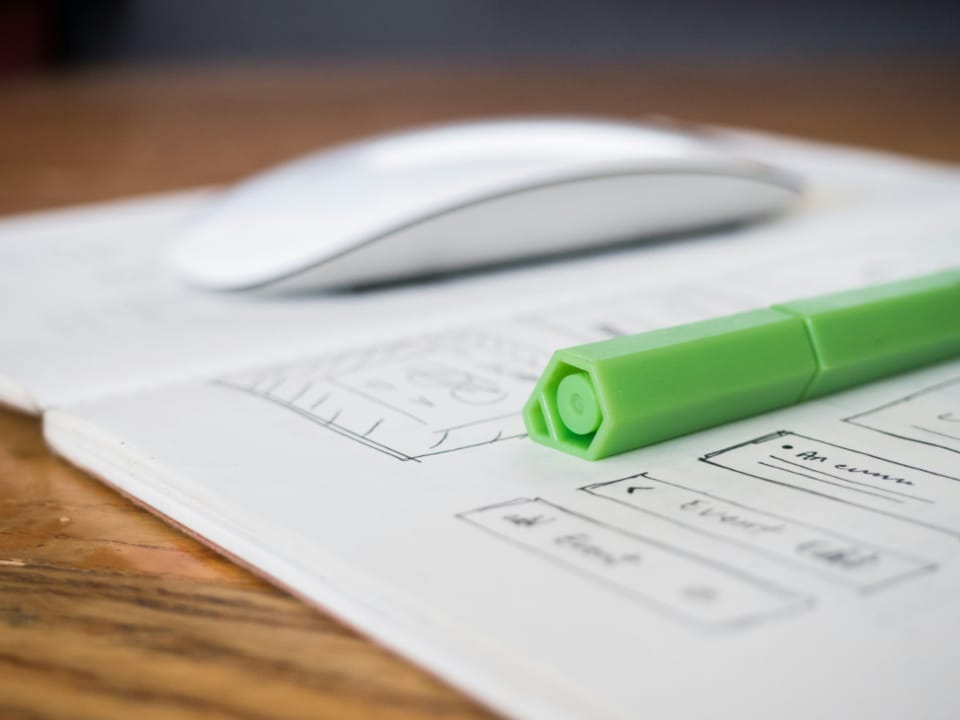 a computer mouse resting on a paper wireframe sketch, representing the transition from design planning to a working website